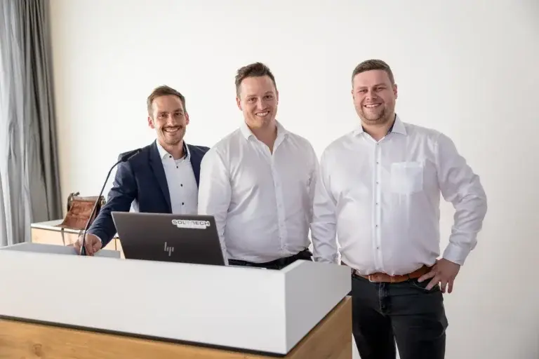Die drei Gründer stehen lächelnd am Rednerpult vor dem Publikum des Infoabends „Connecting the dots“.