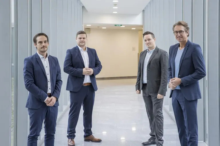 Die drei Gründer stehen gemeinsam mit einem Vertreter der Salzburg AG in einem hellen Gang.