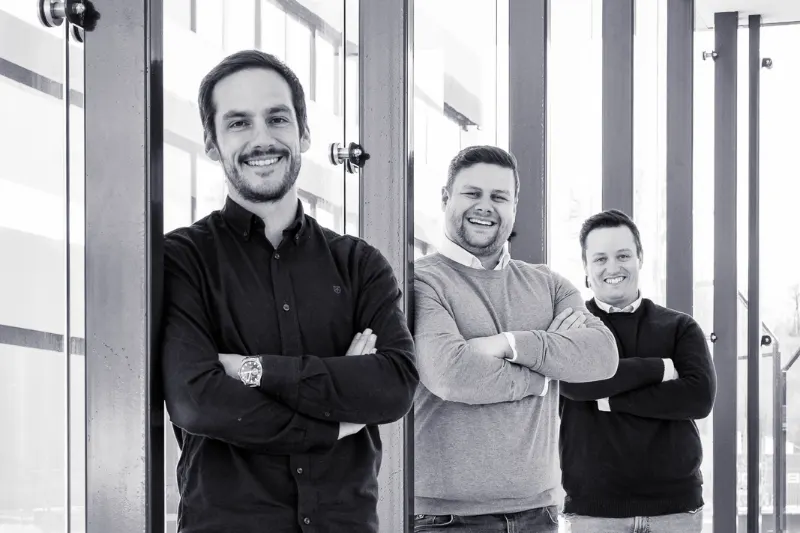 Die drei Gründer der solbytech gmbh – Florian Dodegge, Manuel Dorfer und Gerald Eder – stehen lächelnd mit verschränkten Armen nebeneinander.